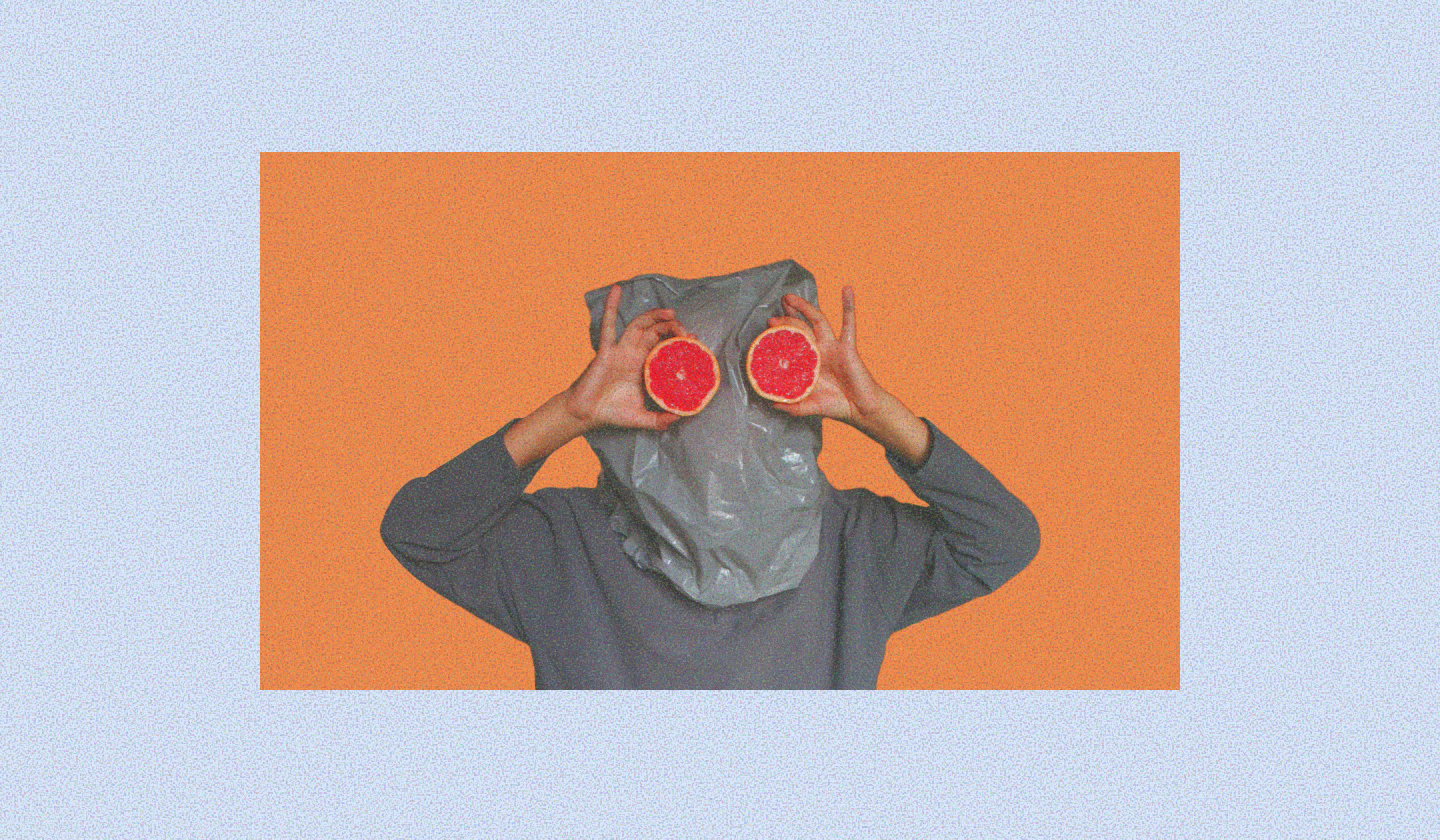 Person with a gray plastic bag over their head holding two halves of a grapefruit in front of their eyes, set against an orange background with a light blue border.